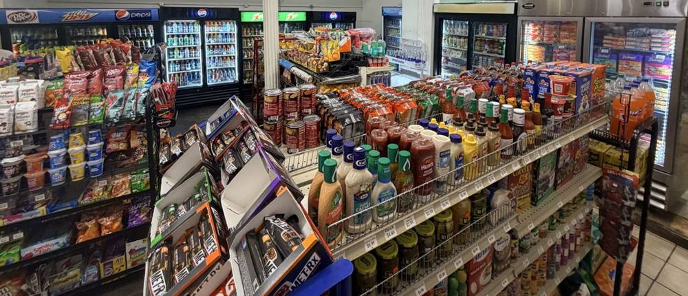 Coolers of soda and water behind a shelf of sauces, cereal and canned food